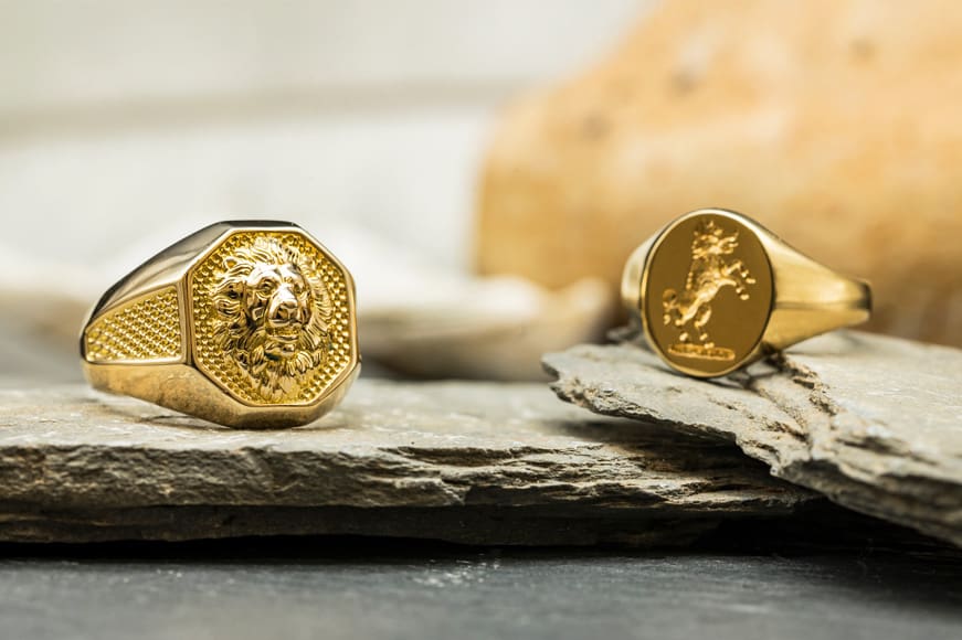 Two yellow gold signet rings embossed with designs of a wolf/dog and a lion, sat upon slate